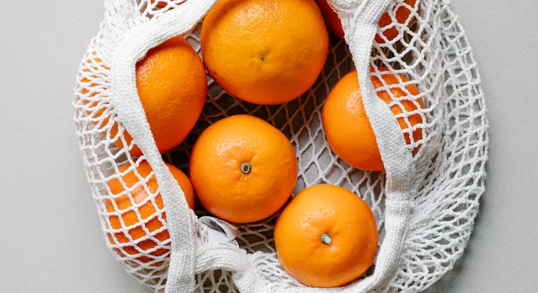 Oranges in a reusable white mesh bag on a light gray background