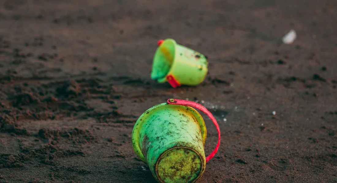 Two green plastic cups on muddy ground, one cup tipped over with a pink handle visible.