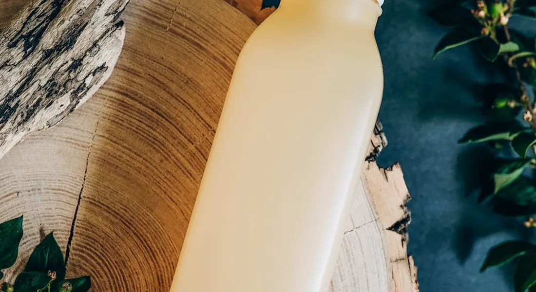 Cream-colored plastic bottle resting on a wooden surface with green foliage in the background.