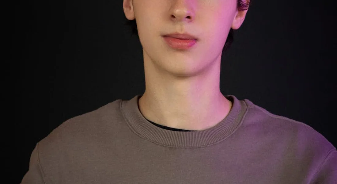 Portrait of a person against a dark background, illuminated by pink and purple lighting.