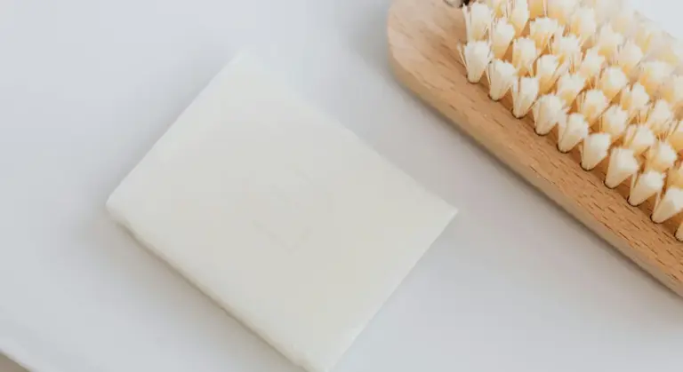 Bar of white soap and a wooden bristle brush on a light surface, representing natural cleaning tools for guinea pig cages.