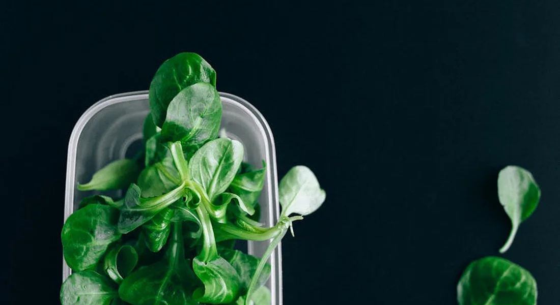Fresh spinach leaves in a clear container against a dark background.