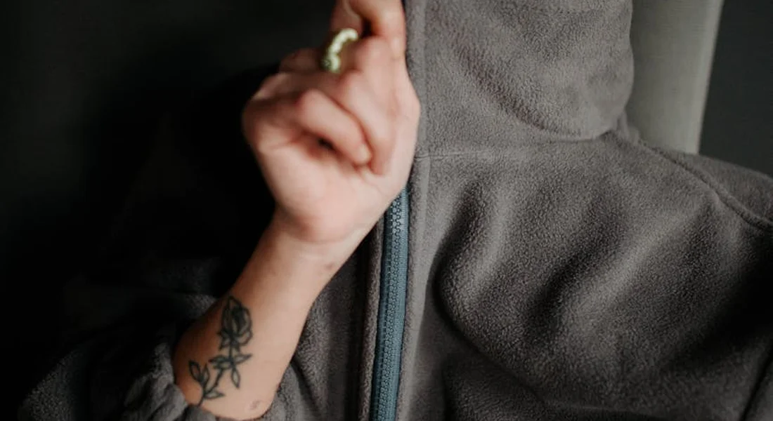 Close-up of a person wearing a gray fleece jacket with a visible zipper and a tattoo on the forearm.