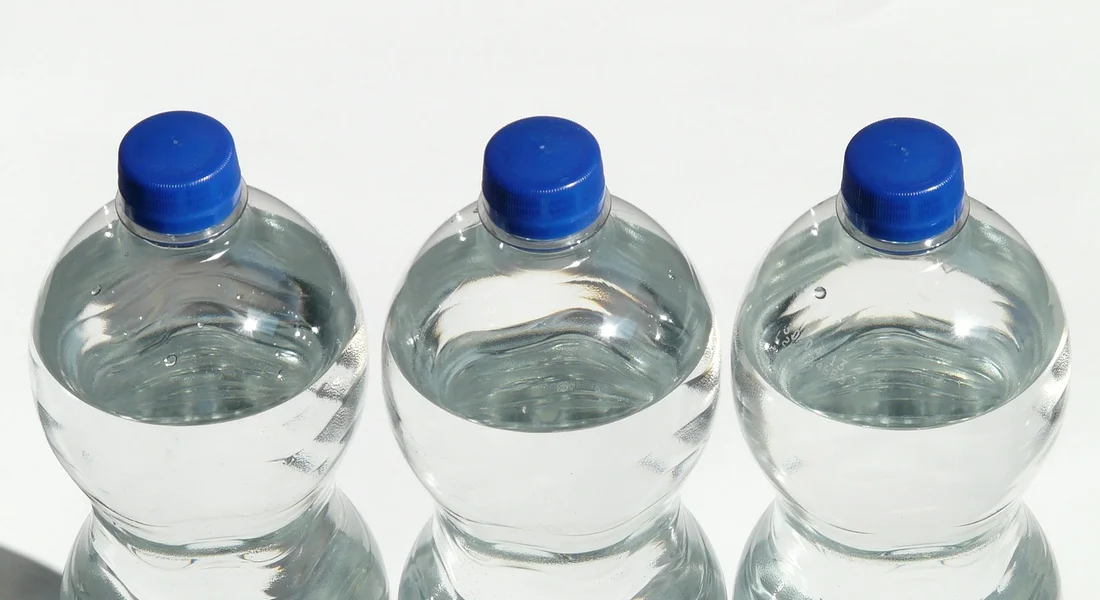 Three clear plastic water bottles with blue caps arranged in a row on a white background
