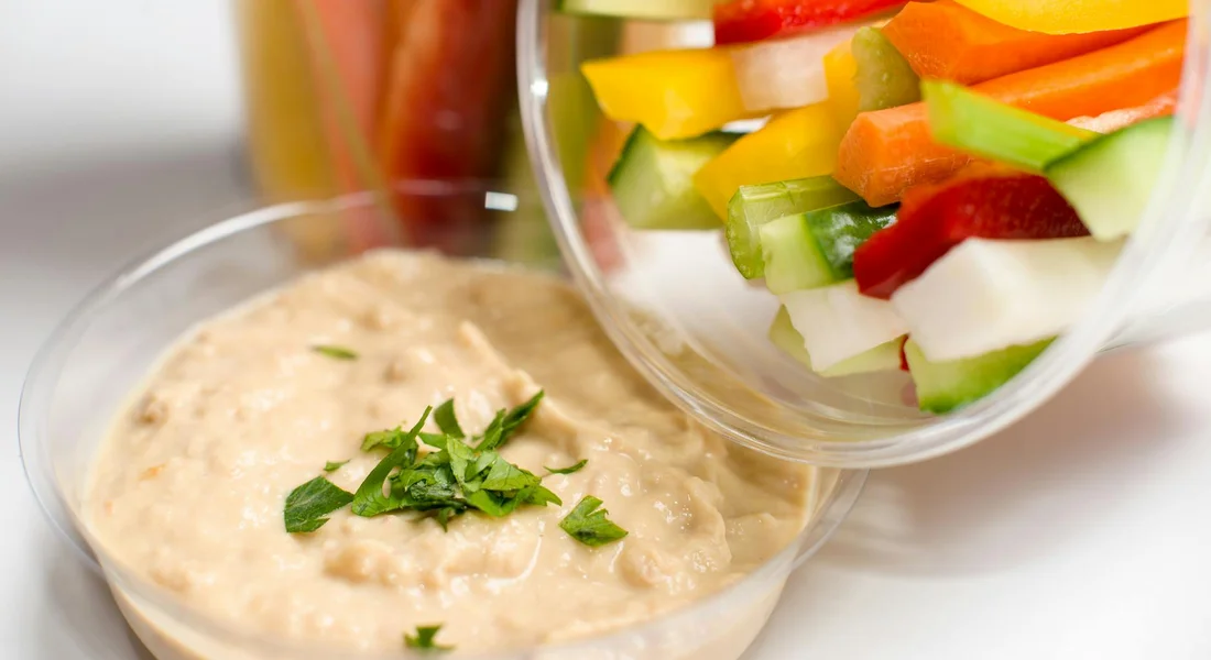 Colorful chopped vegetables for dipping, including celery, bell peppers, cucumber, and carrot, arranged beside a bowl of creamy dip.