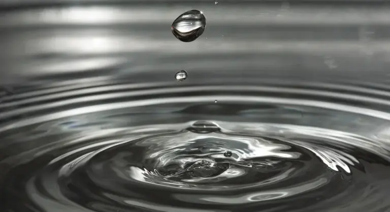 Close-up of a water droplet falling onto a calm water surface, creating ripples