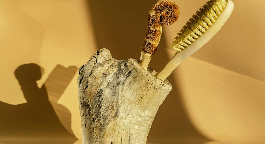 Weathered wooden stump with two cleaning brushes tucked into it against a warm yellow background.